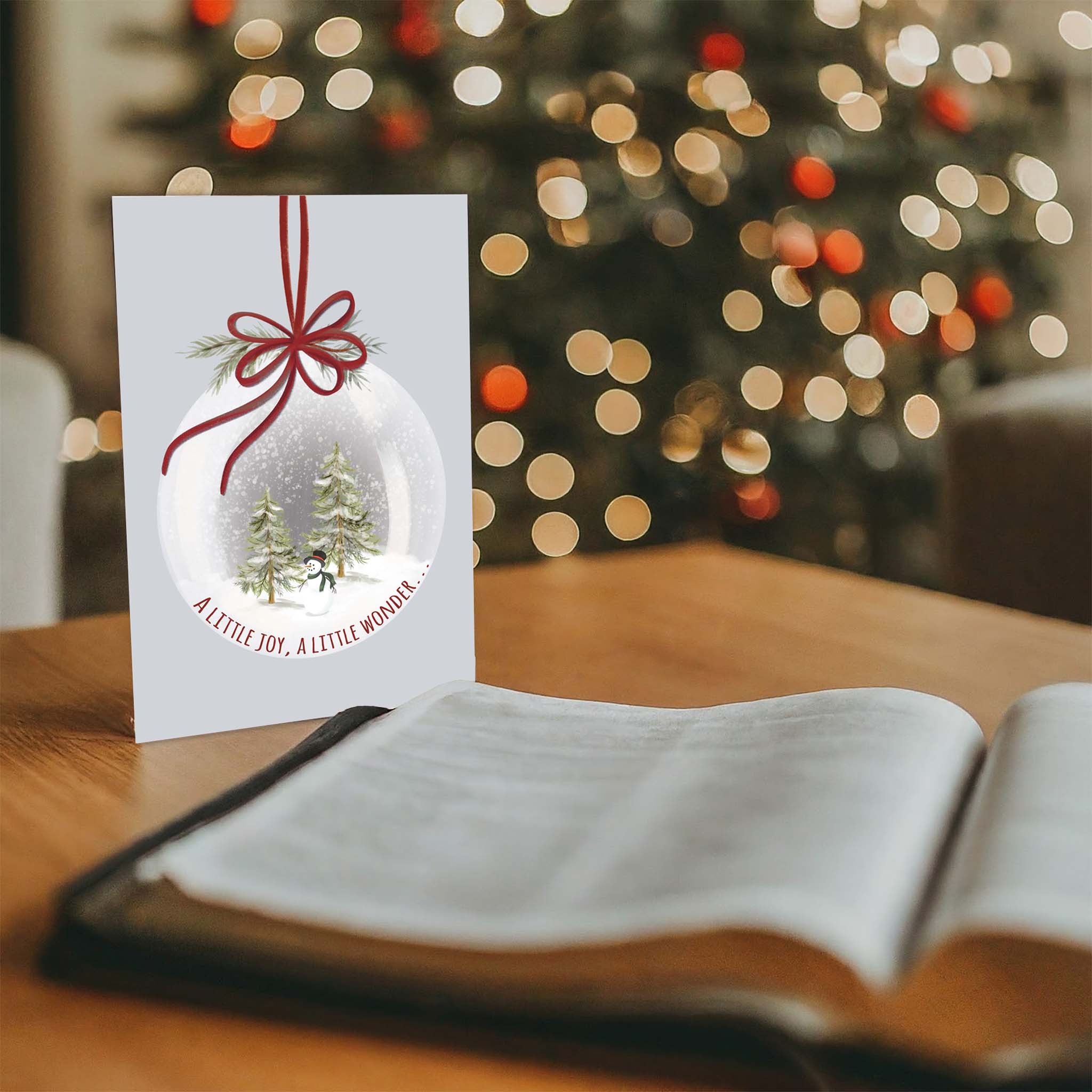 Christmas Snow Globe card on desk with Bible and Tree in backgroun