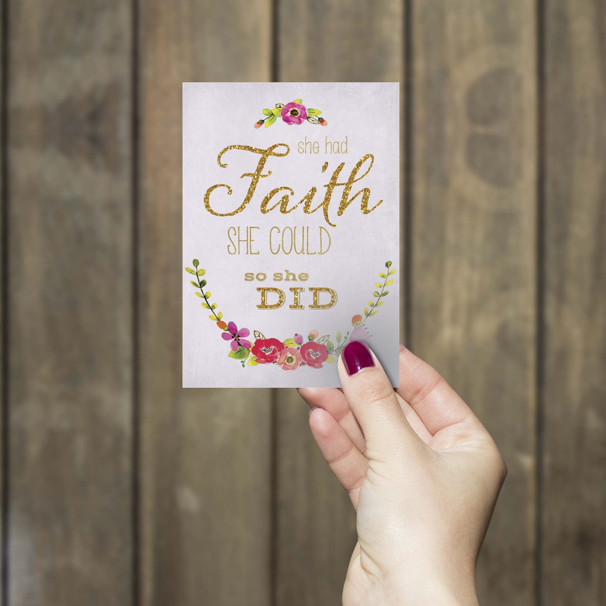 Hand holding a card with 'She had faith she could so she did' text against a wooden background