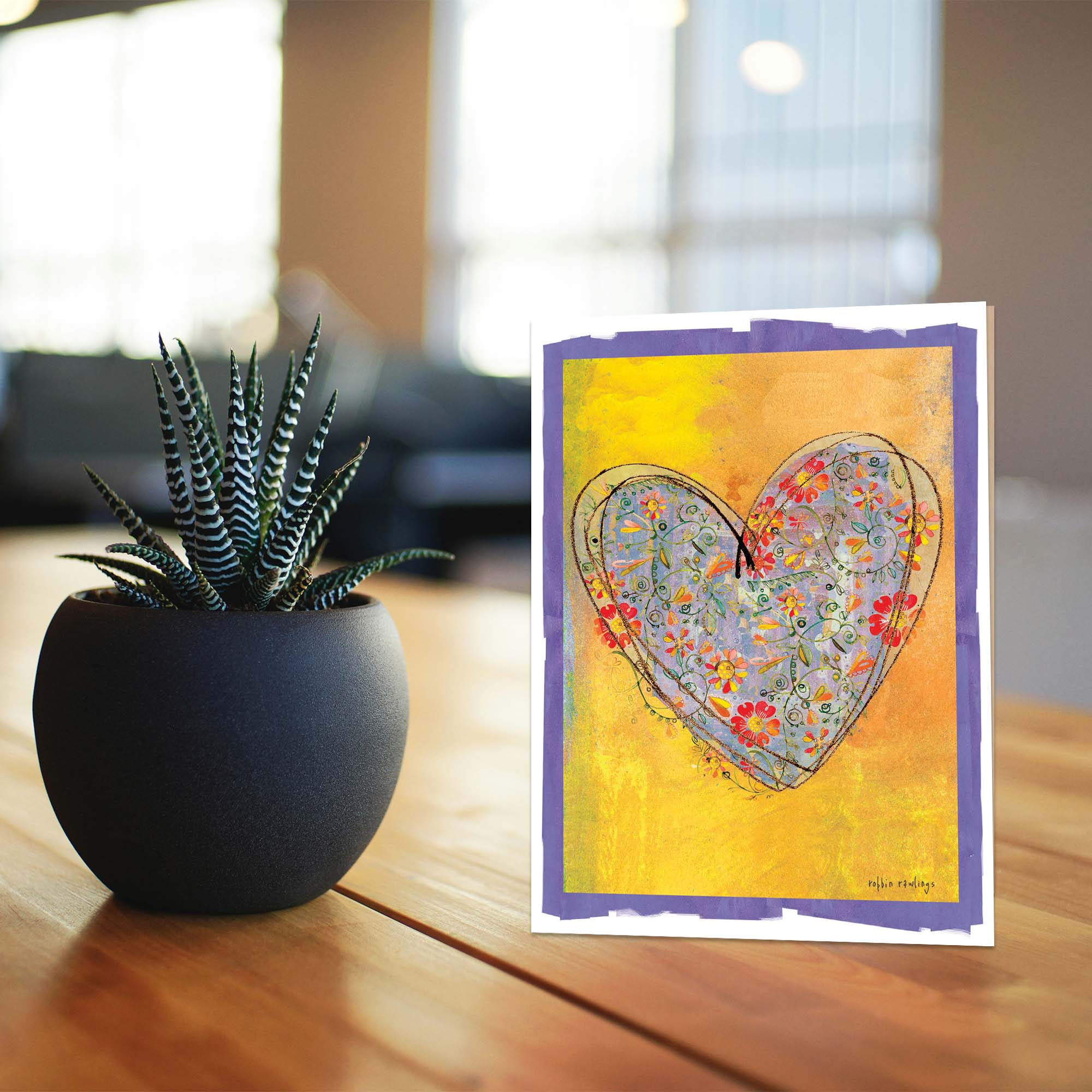 Card with heart design on a wooden surface next to a small potted plant