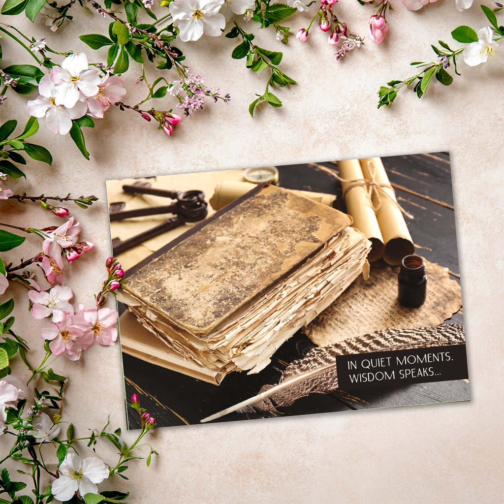 Vintage book with quill pen and inkwell on a card, surrounded by flowers and greenery.
