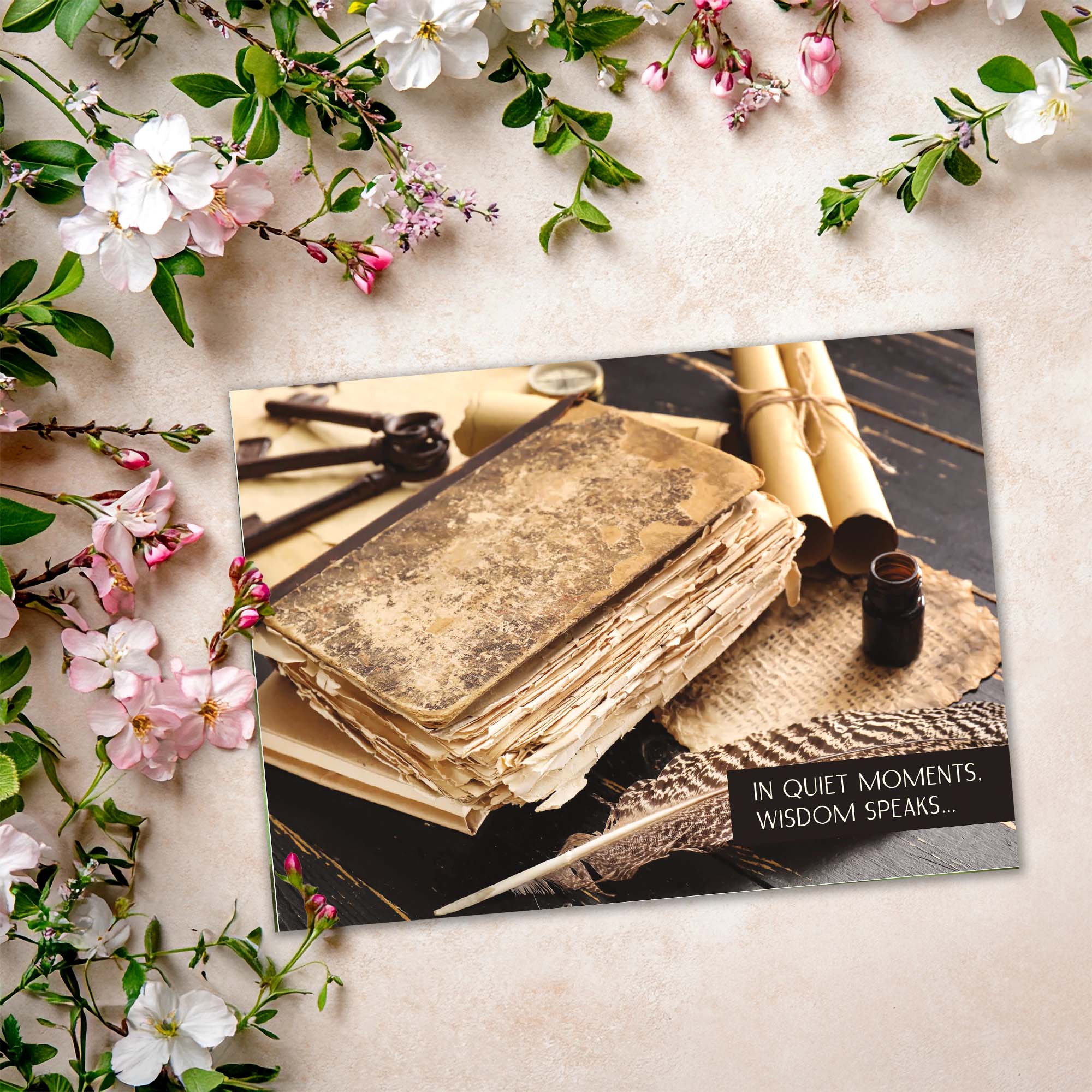 Vintage book with quill pen and inkwell on a card, surrounded by flowers and greenery.