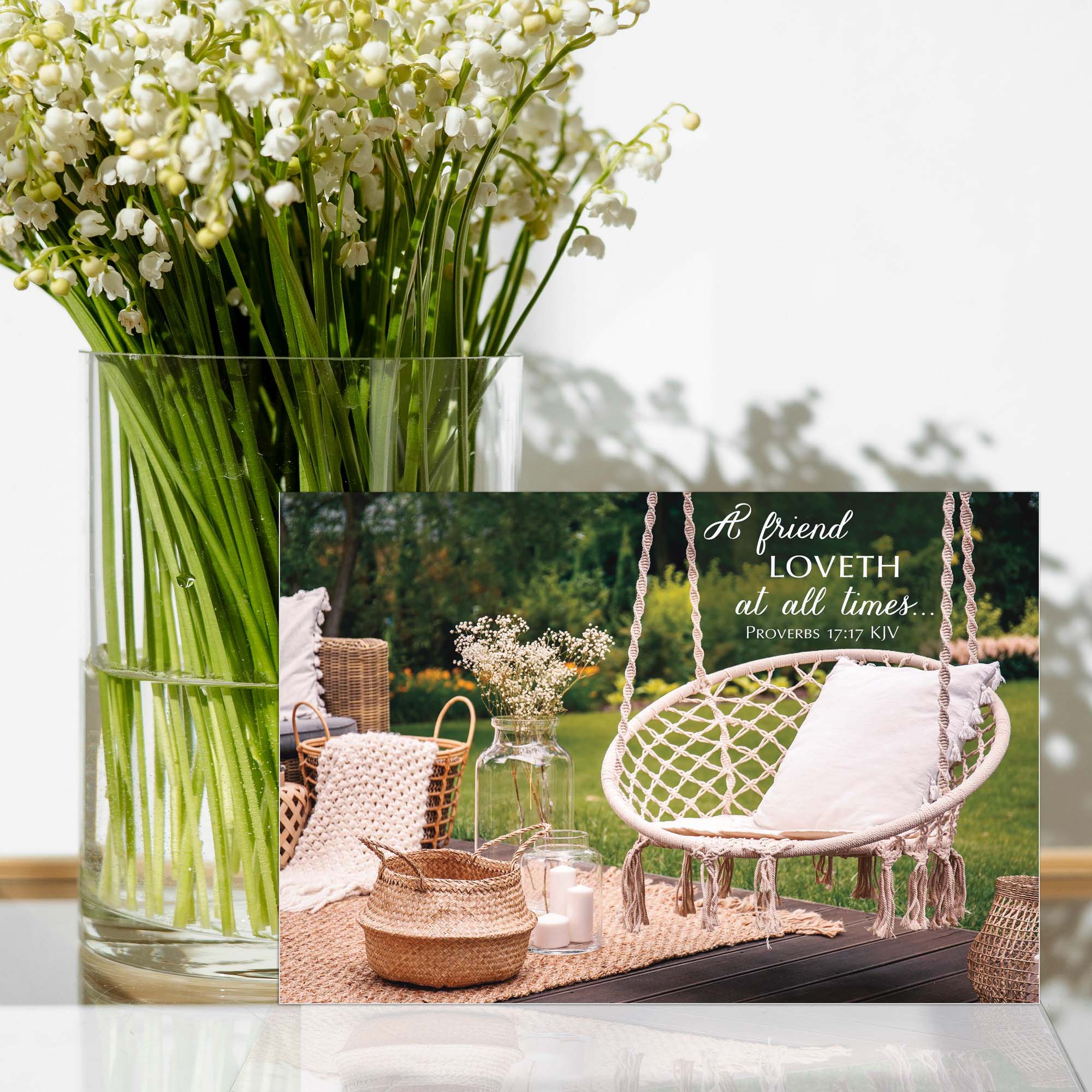 Clear vase with white flowers on a table, with a background of a hammock swing and outdoor setting.