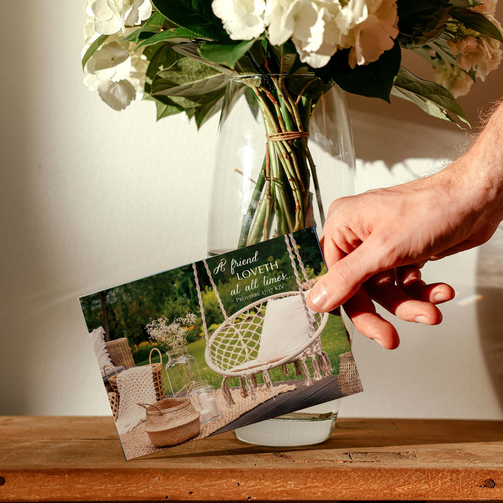Hand holding a card with a garden scene and flowers in the background