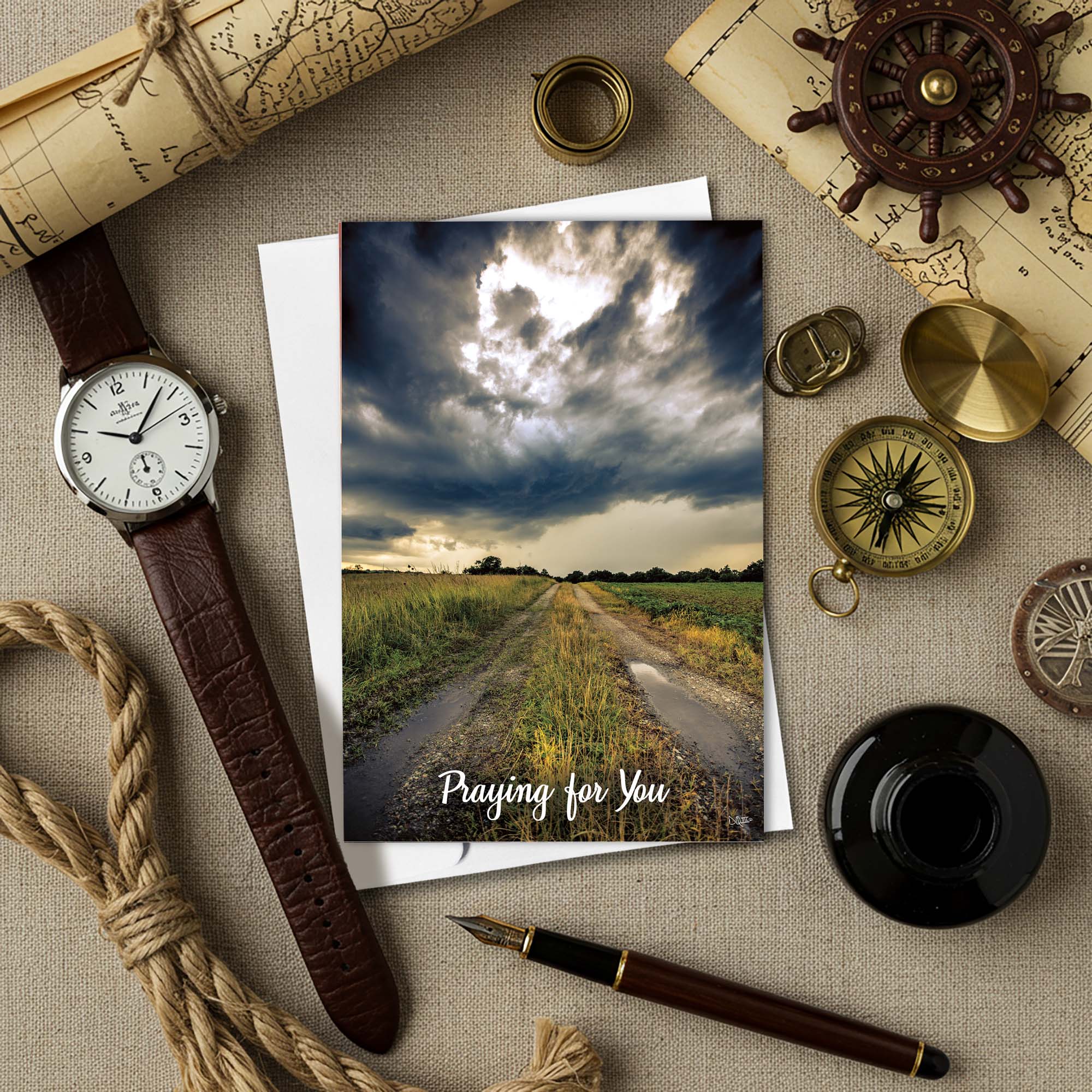Greeting card with a landscape and 'Praying for You' message, surrounded by vintage items on a textured surface.