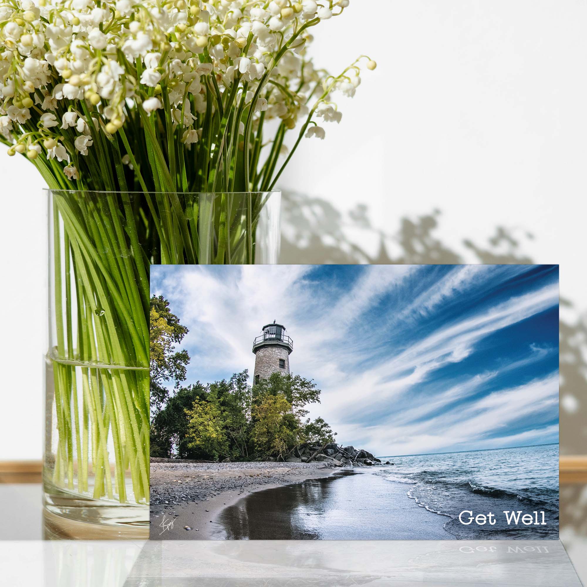 Vase of white flowers with a lighthouse on a beach 'Get Well' card