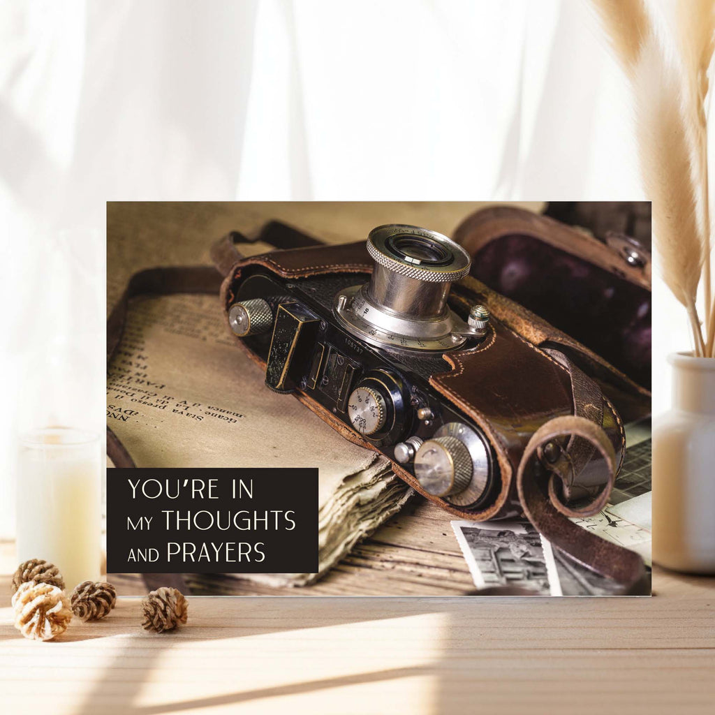 Vintage camera on a surface with text 'You're in my thoughts and prayers' displayed.
