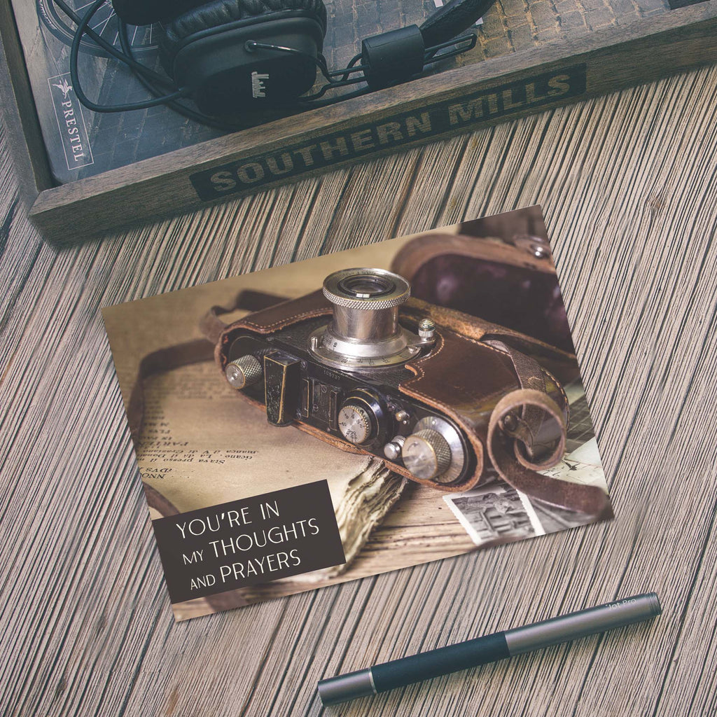Vintage camera-themed card on a wooden surface with a pen and headphones.