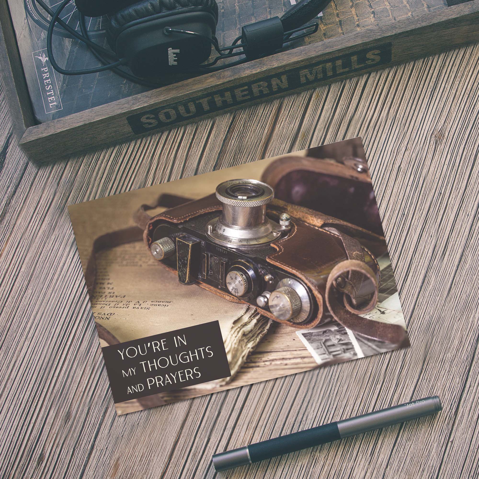 Vintage camera-themed card on a wooden surface with a pen and headphones.