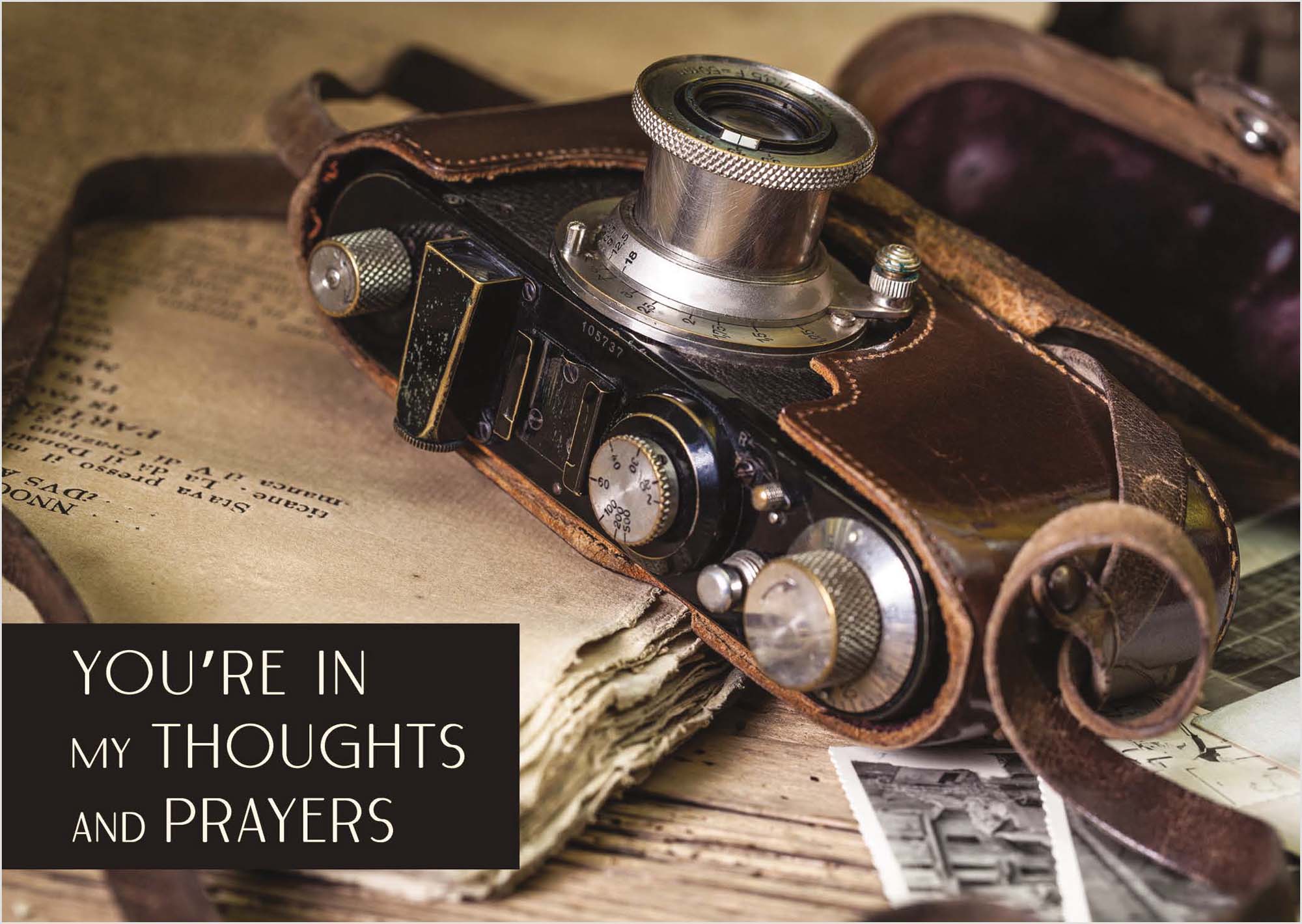 Vintage camera on an old book with text overlay 'You're in my thoughts and prayers'.