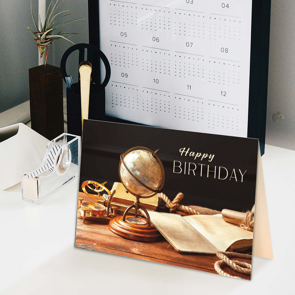 Birthday card with vintage globe and books design on a desk with a calendar in the background.