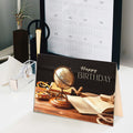 Birthday card with vintage globe and books design on a desk with a calendar in the background.