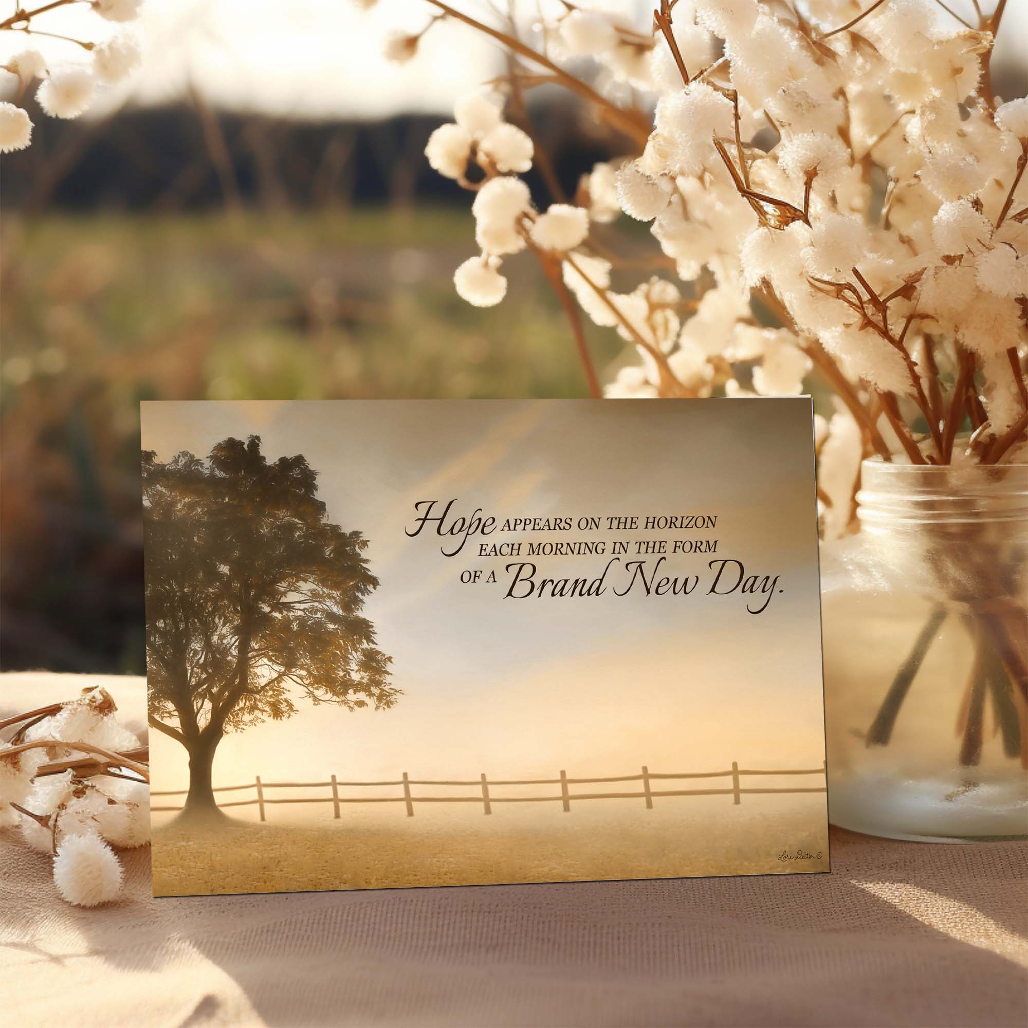 Motivational card with tree and fence illustration and text, placed on a surface with cotton plants.