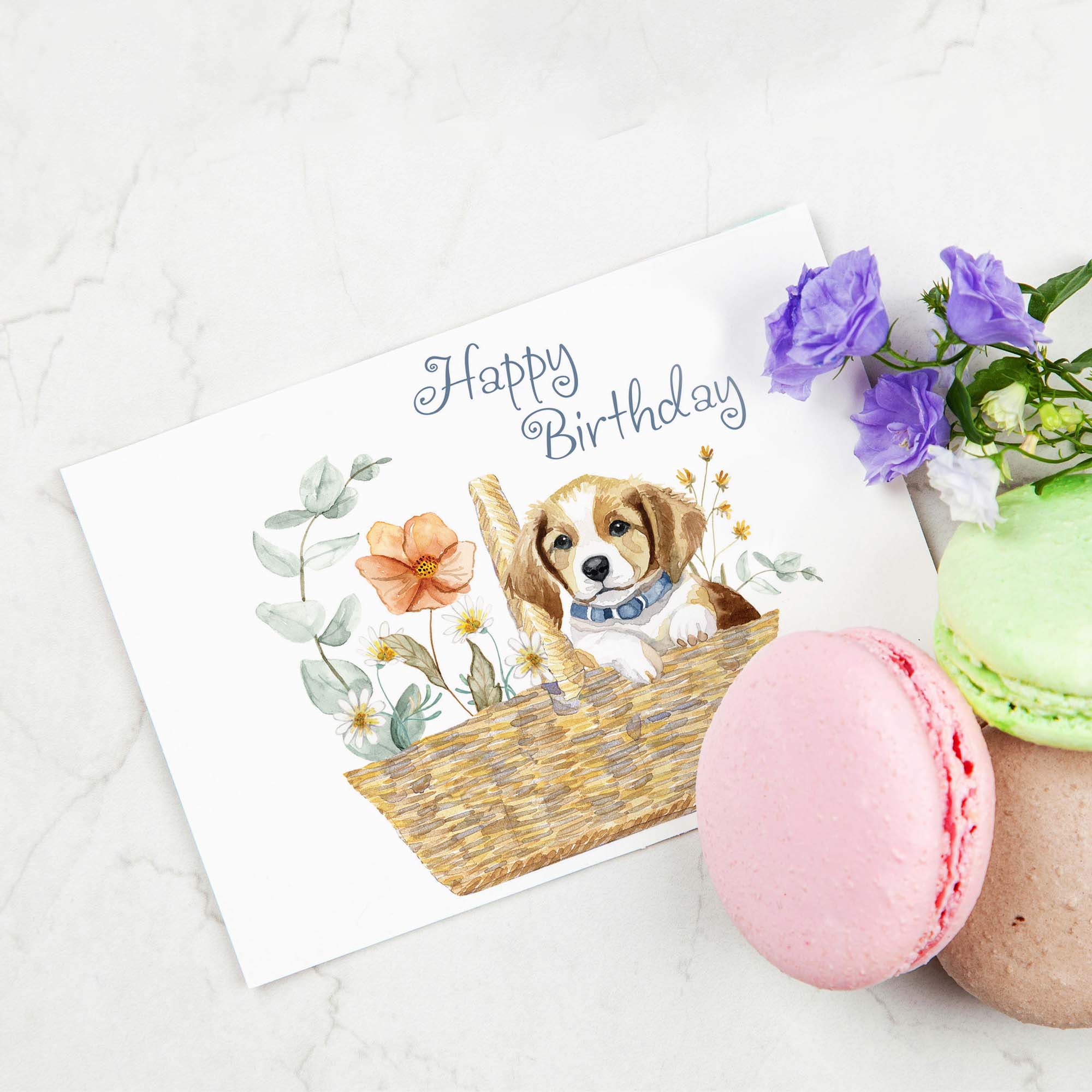 Birthday card with a puppy illustration, flowers, and macarons on a white surface