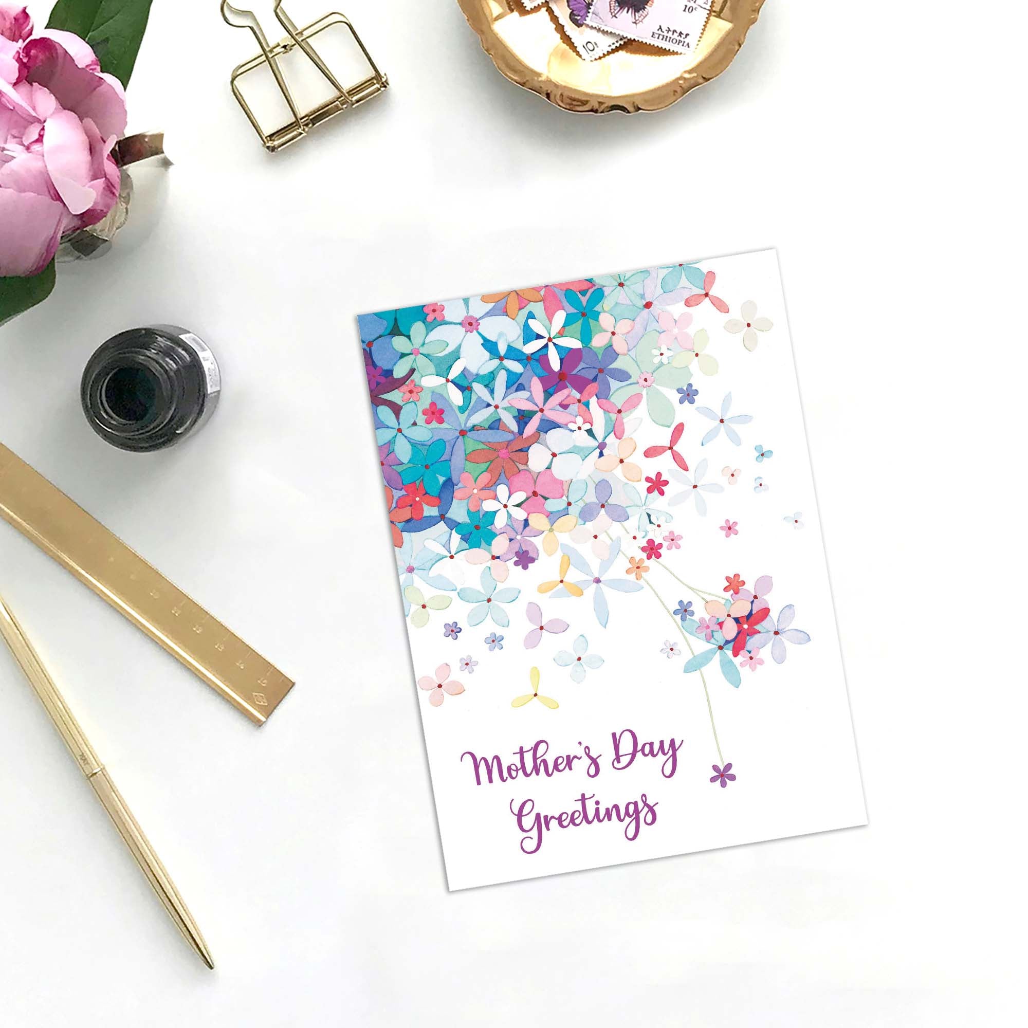 Colorful 'Mother's Day Greetings' card on a white surface with stationery items.