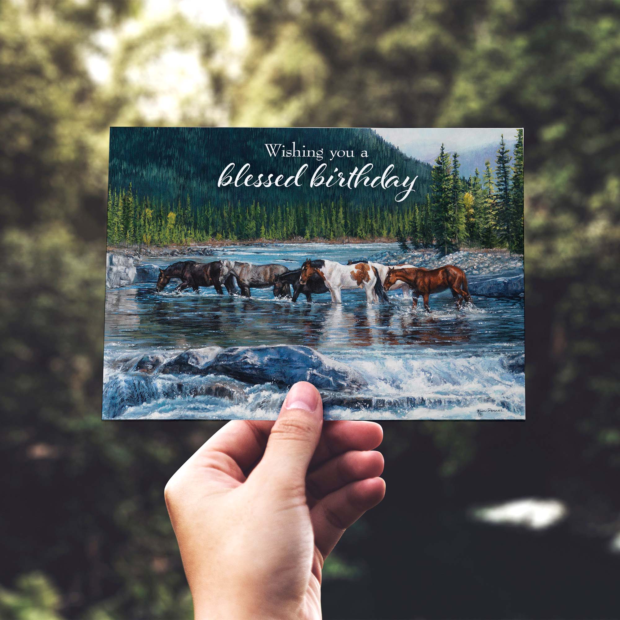Hand holding a birthday card with horses crossing a river and 'blessed birthday' text.