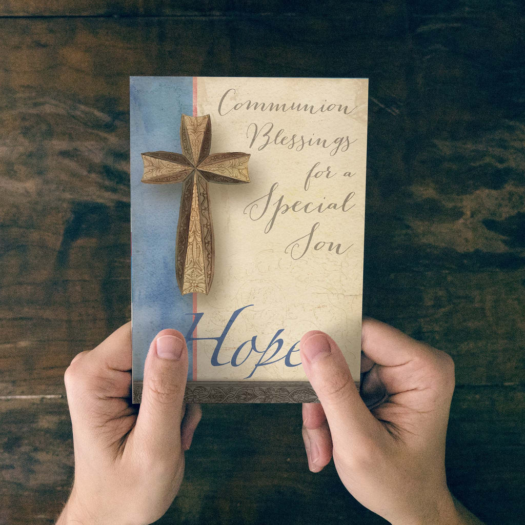Hand holding a card with a wooden cross and text on a wooden surface