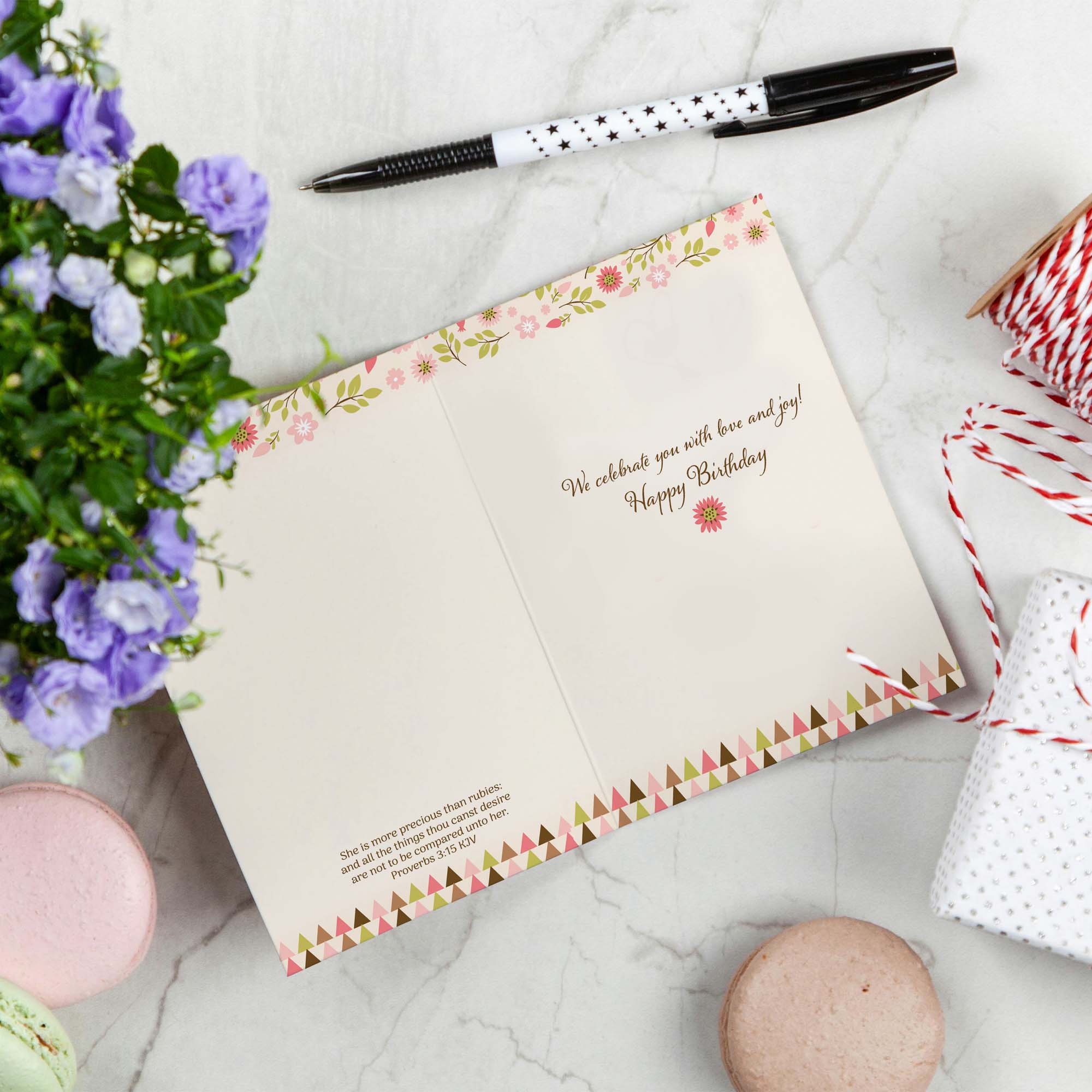 Greeting card with floral design and text, pen, flowers, and macaron on marble surface