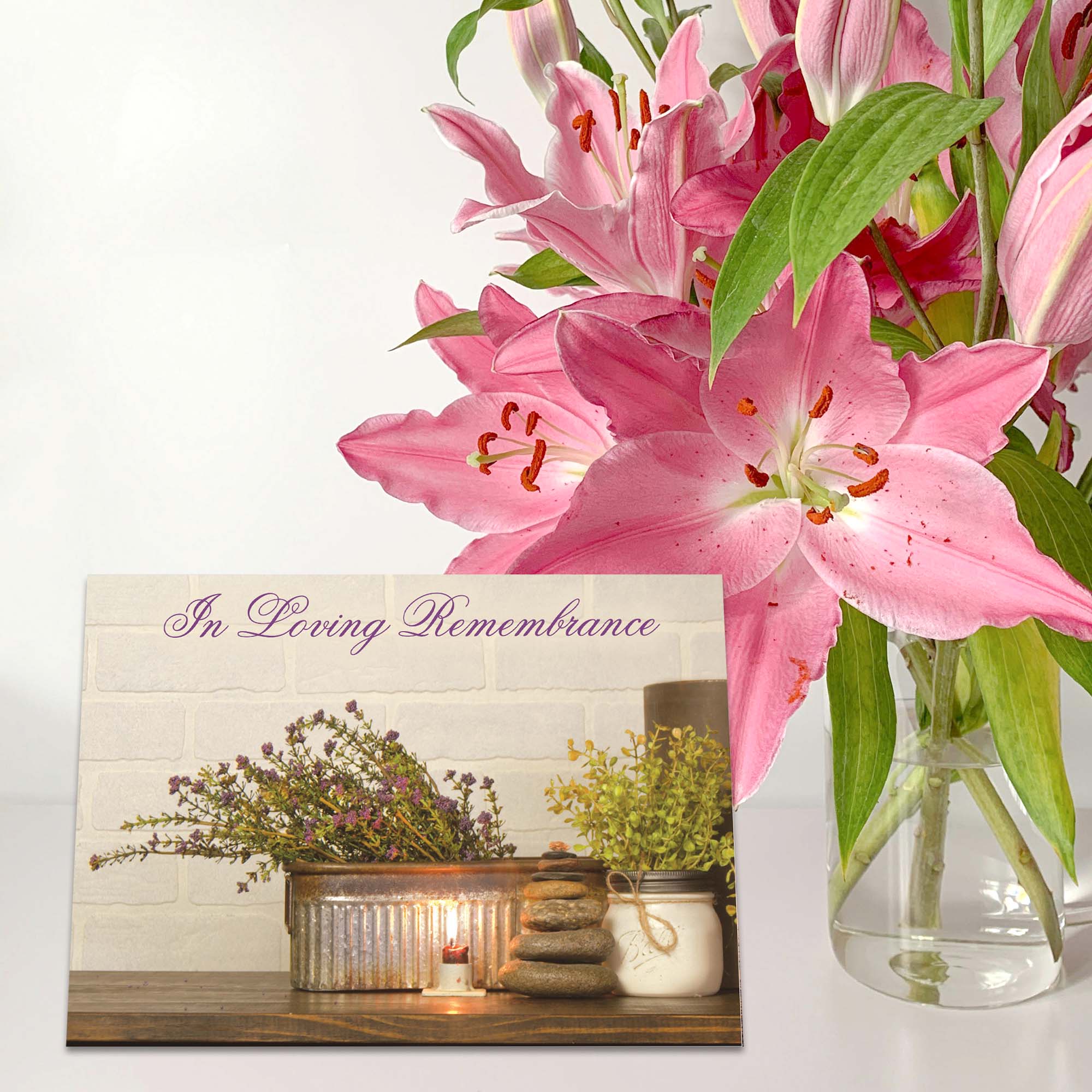 Pink lilies in a vase with a 'In Loving Remembrance' card on a white background