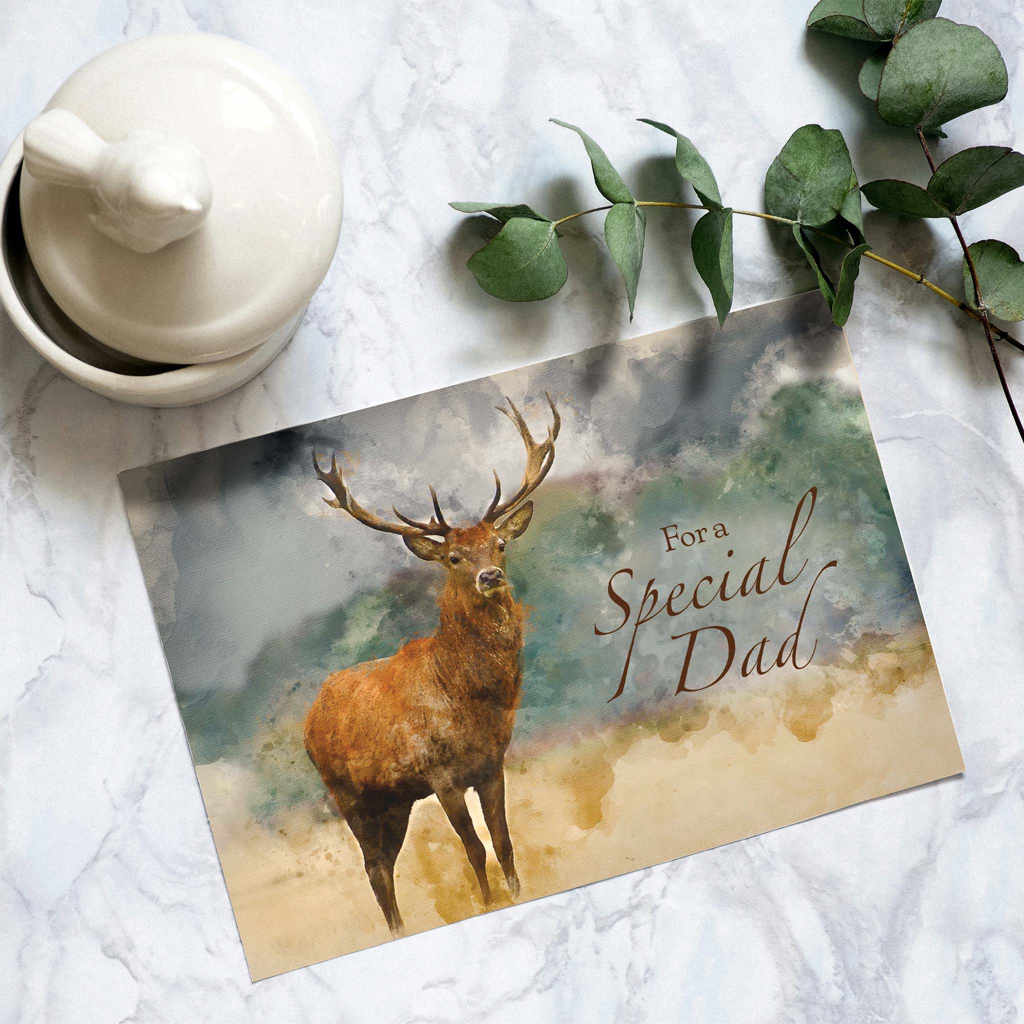 Greeting card with a deer illustration and 'For a Special Dad' text on a marble surface with a teapot and eucalyptus leaves.
