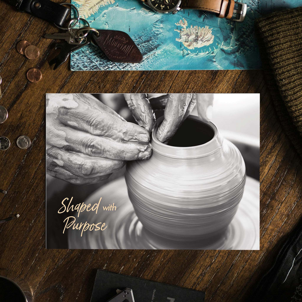 Close-up of hands shaping a pot on a wheel with 'Shaped with Purpose' text, on a wooden surface.