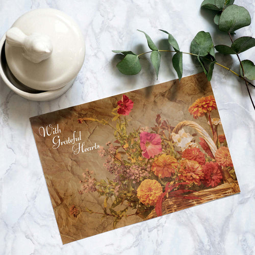 Floral card with 'With Grateful Hearts' text on a marble surface with a teapot and eucalyptus leaves.
